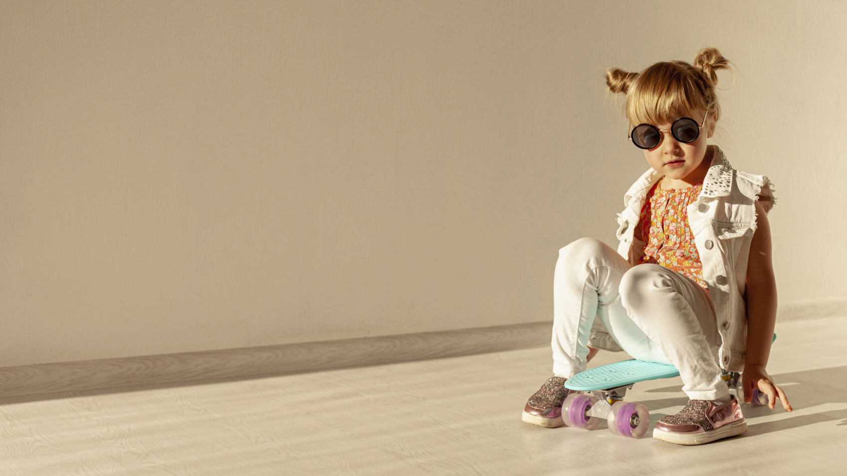 Child sitting on a skateboard indoors.